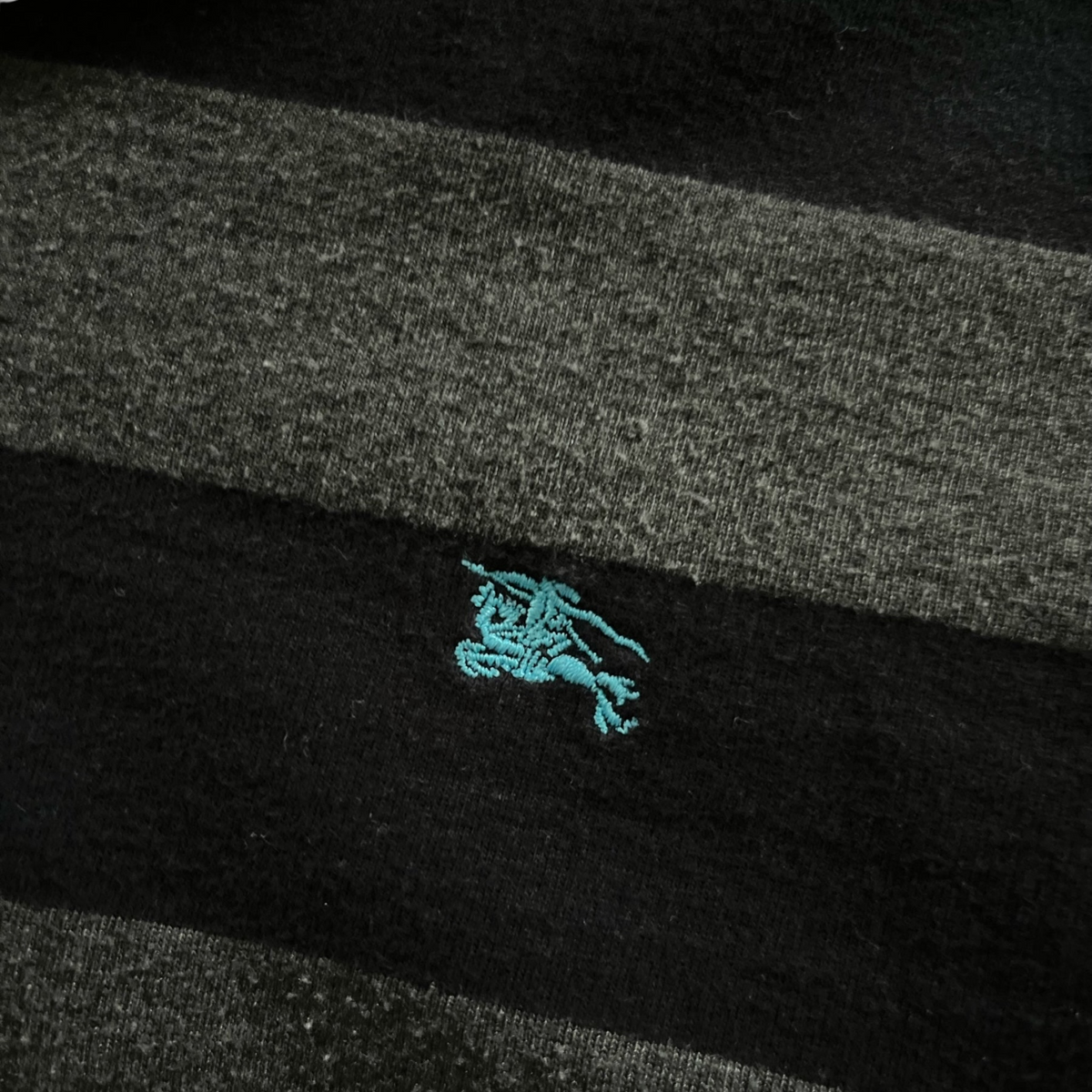 streetcave.eu Burberry Black Label Poloshirt mit schwarz-grauem Streifenmuster und türkisfarbenem Logo-Stick